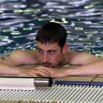 Male swimmer rests at side of indoor pool