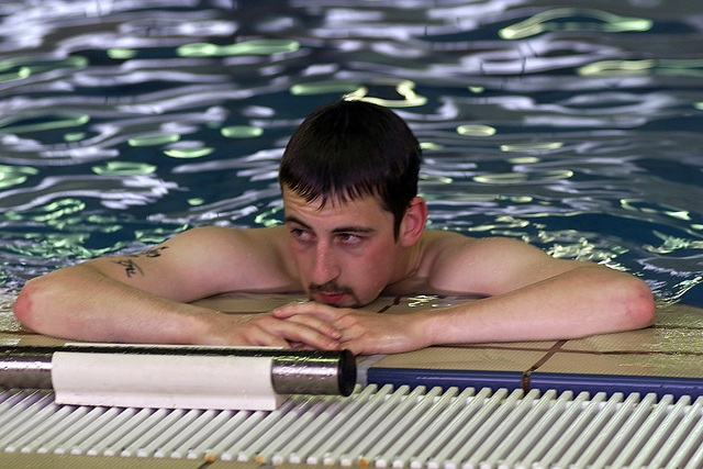 Male swimmer rests at side of indoor pool