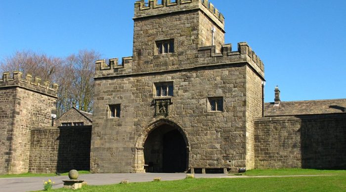 A picture of Hoghton Tower gatehouse and walls, set against a bright blue sky. There is a grassy lawn in front of the wall with a stone pathway next to it.