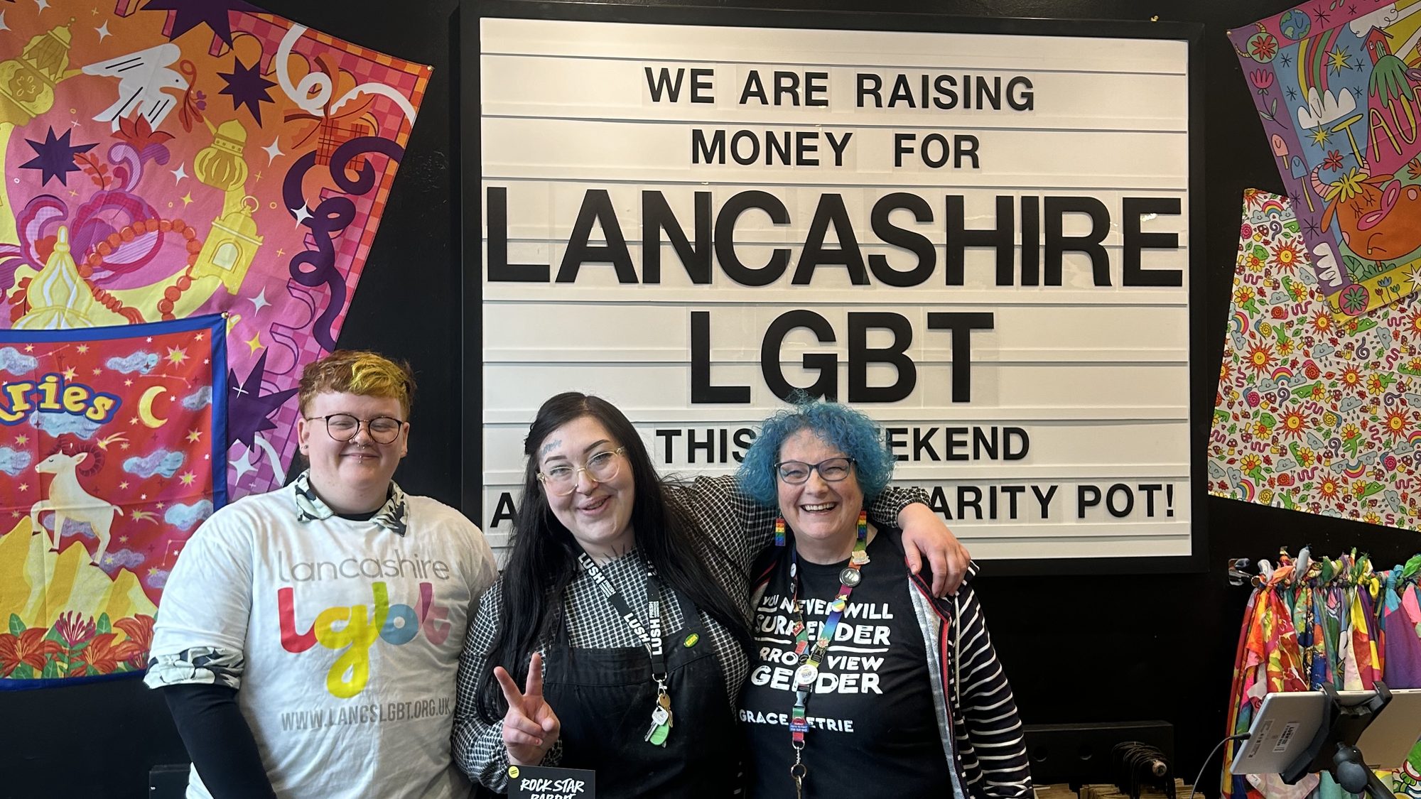 Three volunteers in front of a sign reading We are raising money for Lancashire LGBT this weekend